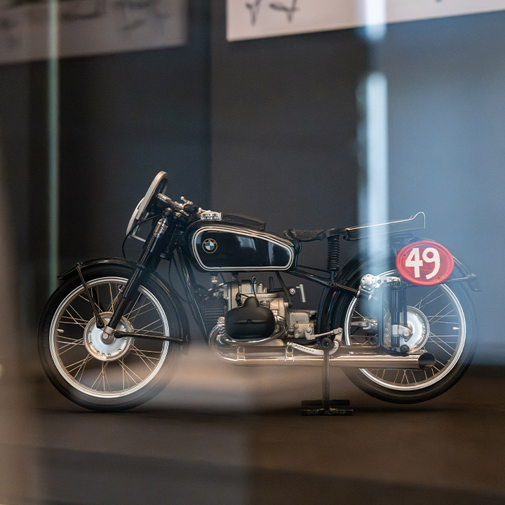A BMW motorcycle is on display in a glass cabinet, attracting the attention of onlookers.