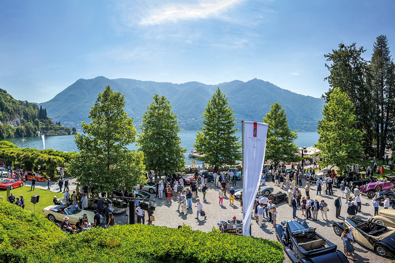 Vintage cars and their owners in the parking lot in front of the Hotel Villa d’Este with lake and mountains in the background