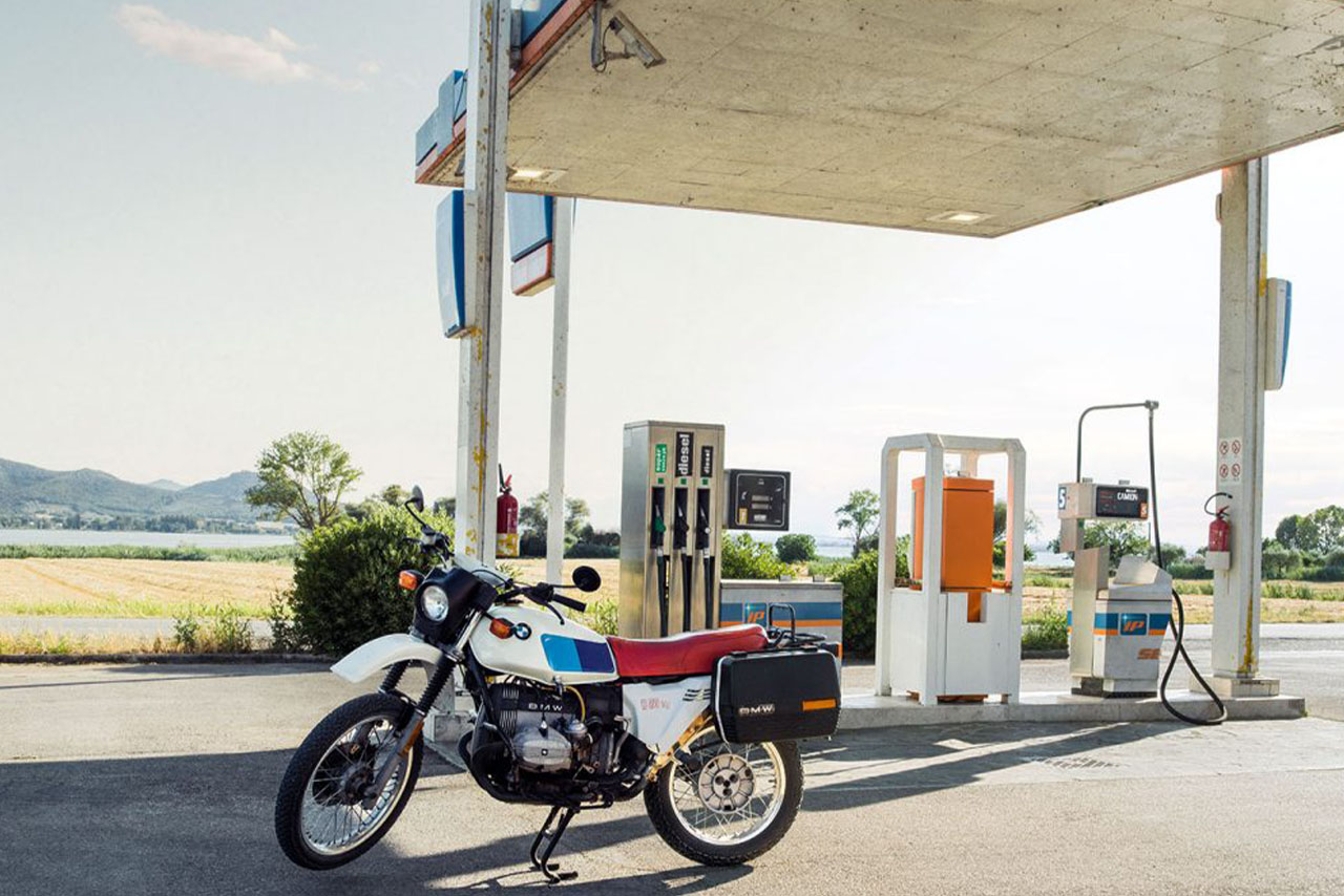 A BMW motorcycle parked next to a gas station, surrounded by tranquil surroundings.