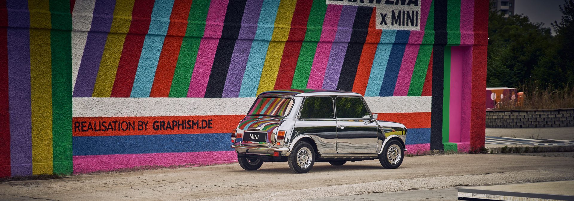 Historic, silver MINI standing in front of a colorful striped wall