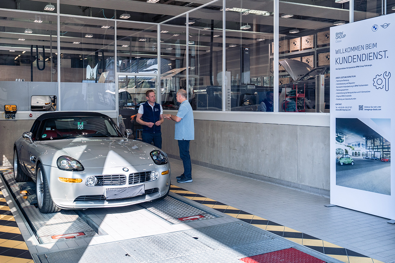 Two men stand next to a BMW sports car and pose for a photo.
