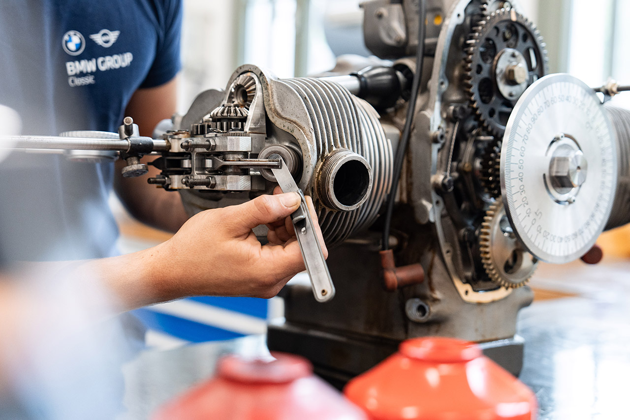 A mechanic repairs a BMW motorcycle engine, surrounded by tools and spare parts.
