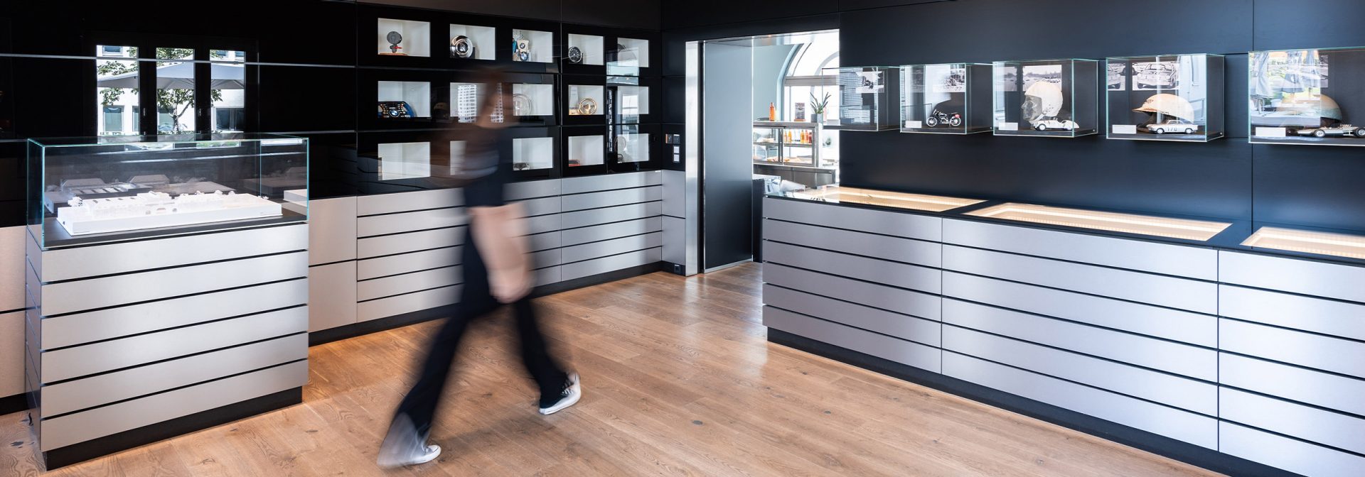 A person walks through the BMW Classic Archive with numerous glass cabinets displaying various products.