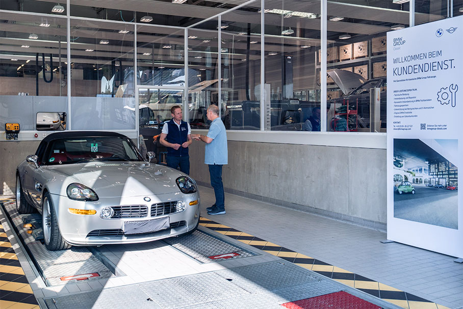 In a garage, two men stand next to a BMW Classic car and seem to be exchanging ideas.