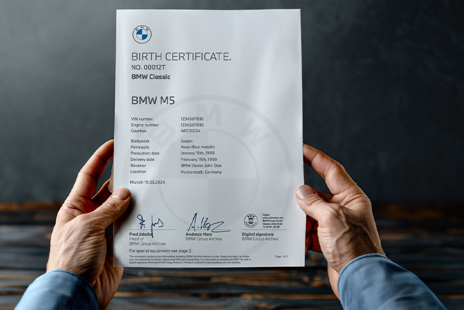 Two hands holding the BMW Birth certificate of a BMW M5