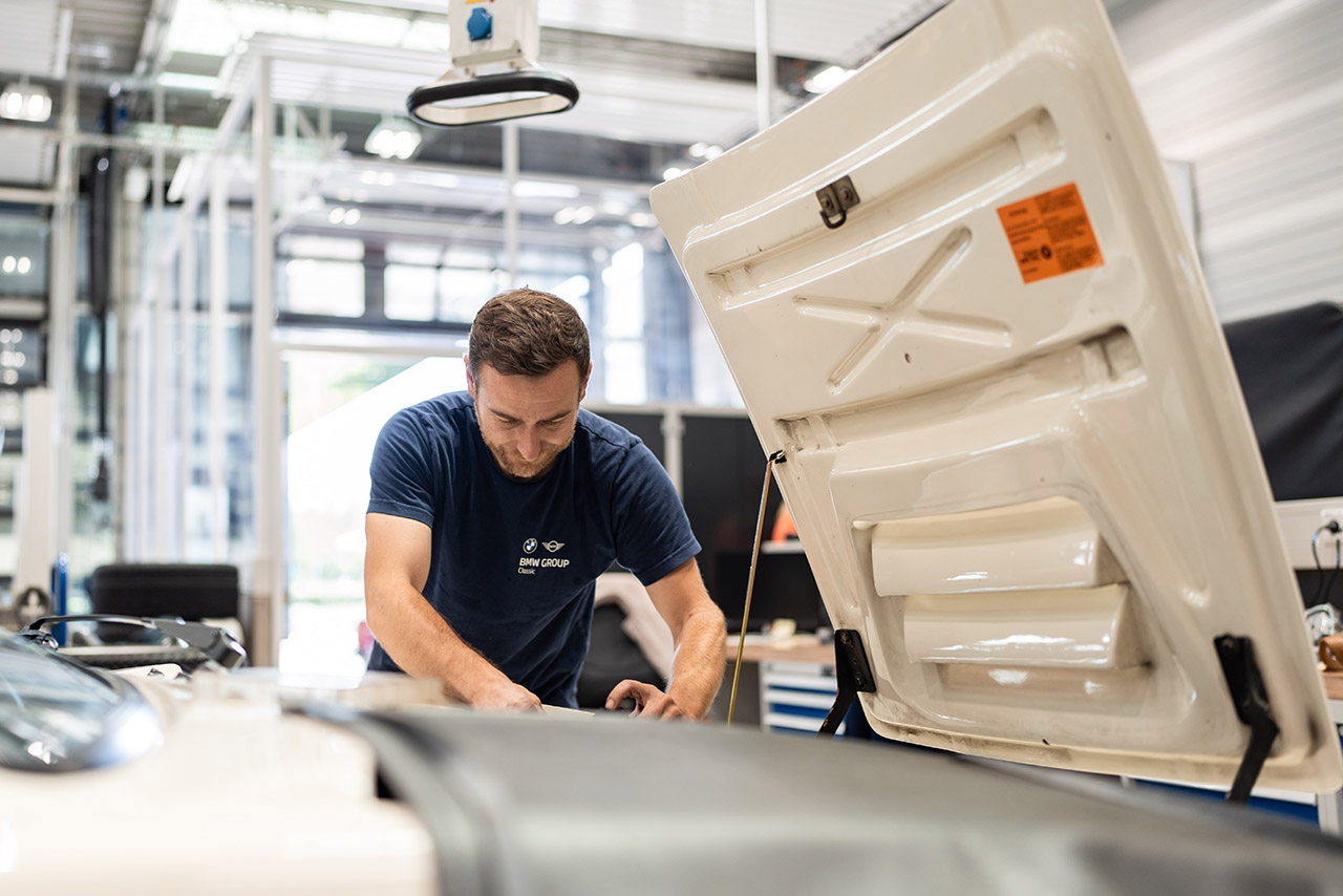 A man performs maintenance on a BMW Classic model in a garage surrounded by various tools.