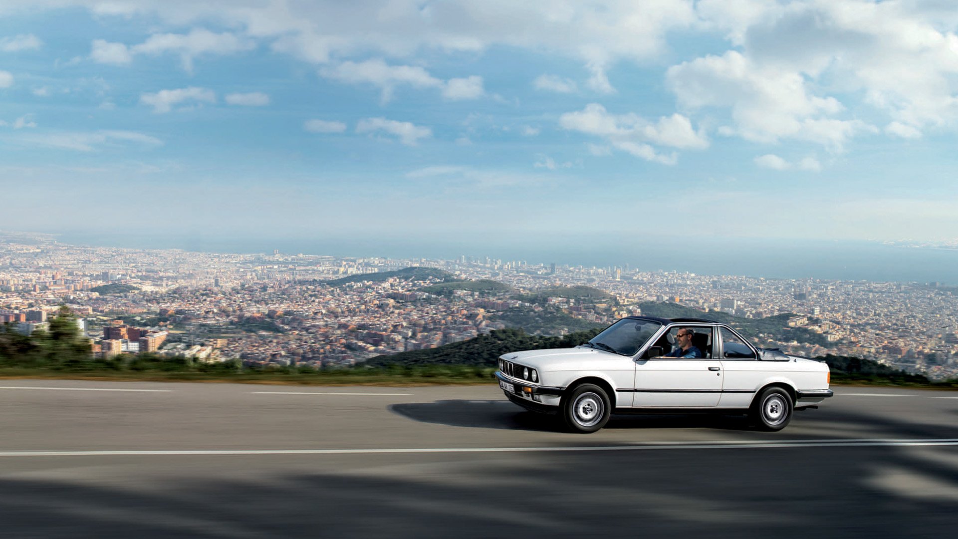 White BMW 3 series (2nd generation) on a mountain road overiewing a city