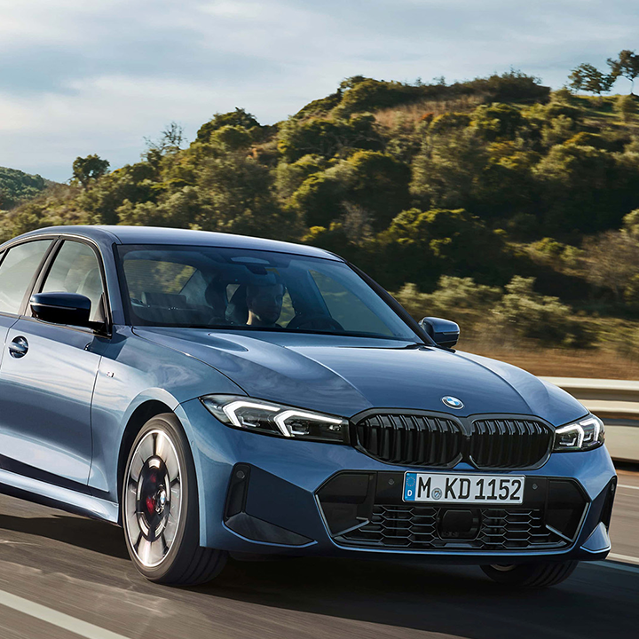 Front view of a blue BMW 3 series driving on a scenic road