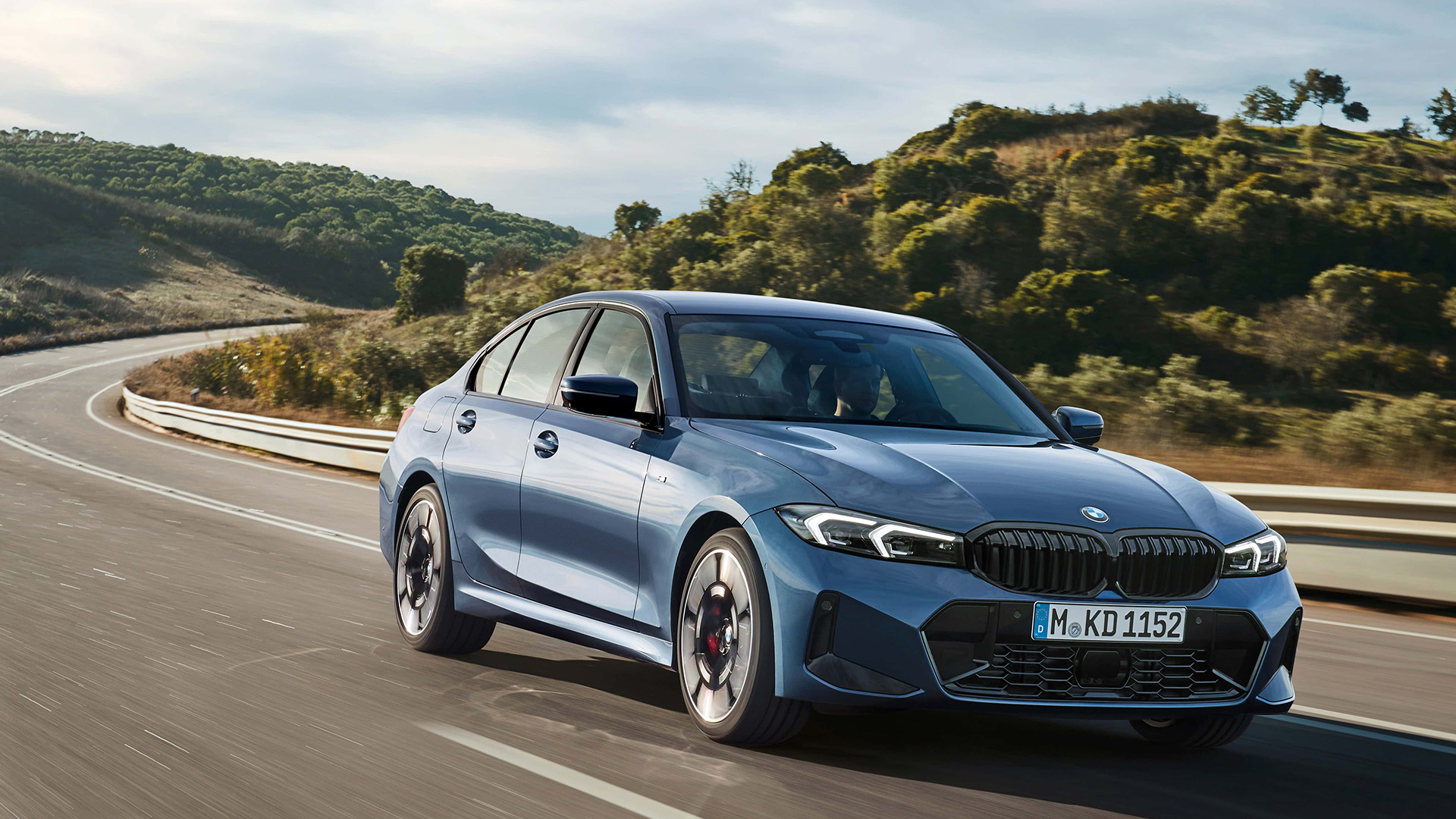 Front view of a blue BMW 3 series driving on a scenic road